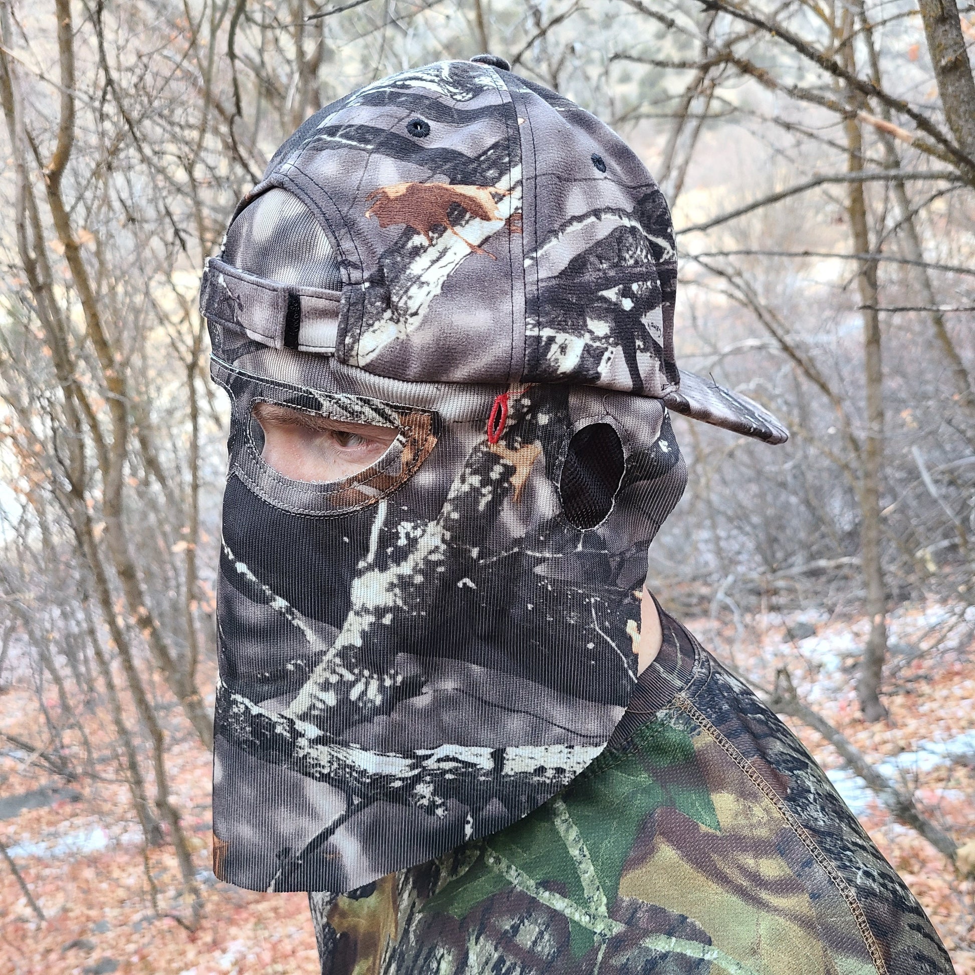 Man Wearing a QuikCamo Mathews Lost Camo Hat Backwards with Face Mask. There is a forest or woods in the background